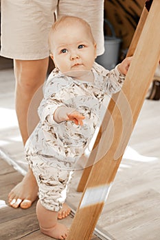 Portrait of cute serious grey-eyed plump cherubic baby infant toddler wearing beige bodysuit with patterns standing.