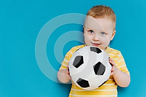 Portrait of cute shy blond little toddler boy in T-shirt holding football ball