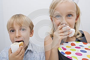 Portrait of cute siblings eating birthday cake slices in house