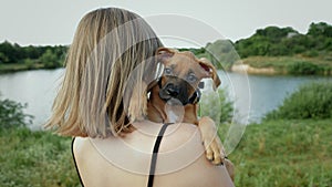 Portrait of cute small german boxer puppy in nature near the lake, woman holds dog on arms
