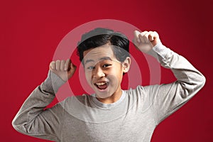 Portrait of cute smart young Asian boy wearing grey shirt shows winning gesture and smiling at camera, celebrating success victory