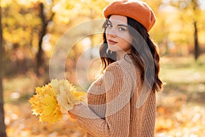 Portrait of cute smiley woman holding autumn leaves walking in the park.