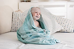 Portrait of cute smiling baby boy covered in big blue towel