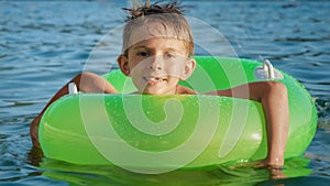 Portrait of cute smiling boy swimming with inflatable ring in sea lit by sunset light. Family holidays, vacations