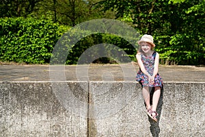 Portrait of cute smiling girl wearing hat sitting on retaining wall