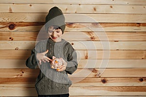 Portrait of cute smiling little boy with piggy bank on wooden background. Child with money in green hat.