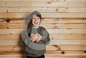 Portrait of cute smiling little boy with piggy bank on wooden background. Child with money in green hat.