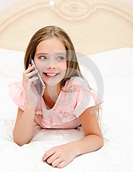 Portrait of cute smiling  little girl child calling by cell phone smartphone lying on the bed