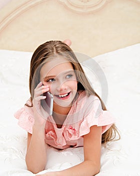 Portrait of cute smiling  little girl child calling by cell phone smartphone lying on the bed