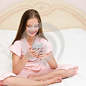 Portrait of cute smiling  little girl child calling by cell phone smartphone sitting on the bed