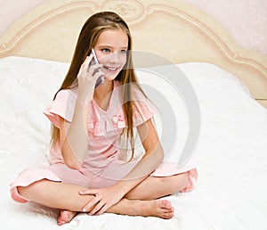 Portrait of cute smiling  little girl child calling by cell phone smartphone sitting on the bed