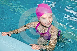 Portrait of cute smiling little girl child swimmer in pink swimming suit and cap in the swimming pool