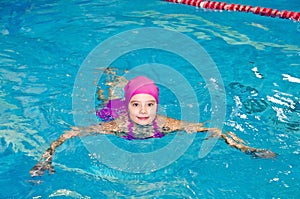 Portrait of cute smiling little girl child swimmer in pink swimming suit and cap in the swimming pool