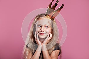 Portrait of cute smiling little girl in princess dress and crown on pink background