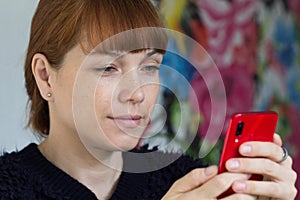 Portrait of the cute smiling middle aged woman looking at mobile phone