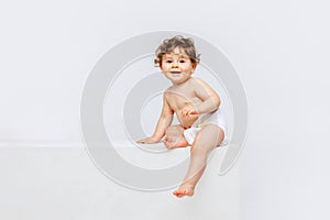 Portrait of cute smiling toddler boy, baby in diaper sitting isolated over white studio background. Happy child