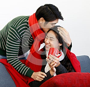 Portrait of cute smiling young Asian lover couple in long sleeve sweatshirt and scarf hugging and relaxing on a couch at home