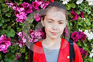 Portrait of a cute smilling girl in a red leather jacket on a background of flowers