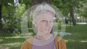 Portrait of cute smilling old woman with grey hair and blue eyes sitting in the green amazing park. Adorable mature