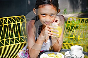 Portrait of Cute Southeast Asian Teenage Girl in Swimsuit with a Glass of Healthy Orange Juice on Hands, Having Meals After