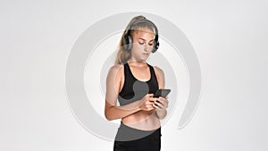 Portrait of cute sportive girl child wearing headphones, using smartphone while posing isolated over white background