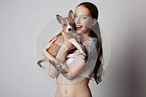 Portrait of a cute tattooed young woman hugging and kissing her little puppy basenji dog. Love between dog and owner