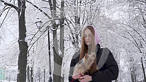 Portrait cute teen girl holding a yorkshire terrier on hands on a background of snow covered trees in a winter park. A