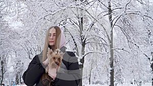 Portrait cute teen girl holding a yorkshire terrier on hands on a background of snow covered trees in a winter park. A