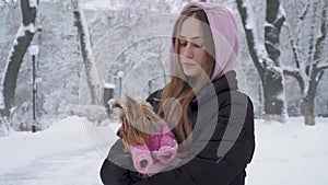 Portrait cute teen girl with long hair hugging a yorkshire terrier dressed in wool sweater holding dog on hands in a