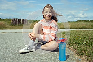 Portrait of cute teenage girl with beautiful smile sitting on ground in sneakers with blue bottle of water