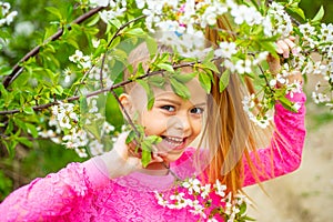 Portrait of cute teenager girl looking at camera surrounded by blooming white cherry branches in garden.