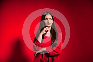 Portrait cute thinking teen girl wearing stylish red costume over red background wall looking away