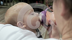 Portrait of cute toddler baby being fed by her mother using bottle. Loving woman giving to drink milk to her chubby son