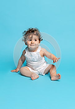 Portrait of cute toddler boy, baby in white romper isolated over blue studio background.