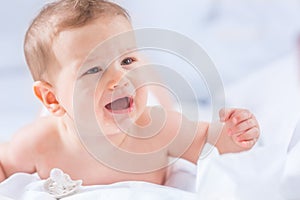 Portrait of cute toddler boy lying on bed. Newborn child in bedroom. Baby lies on his tummy raises the head and crying