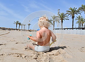 Portrait of a cute toddler boy playing with the sand at the beach in sunlight.