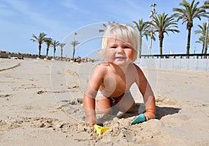 Portrait of a cute toddler boy playing with the sand at the beach in sunlight.