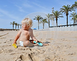 Portrait of a cute toddler boy playing with the sand at the beach in sunlight.