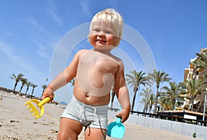 Portrait of a cute toddler boy playing with the sand at the beach in sunlight.