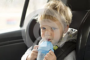 Portrait of cute toddler boy sitting in car seat. Child transportation safety. Adorable baby boy with water bottle