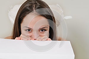 Portrait of cute very shy angel girl hiding behind a white box