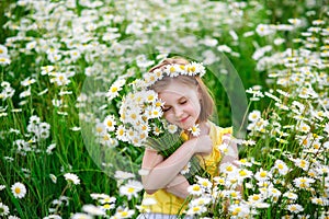 Portrait of a cute village girl in a wreath and a bouquet of flowers on a chamomile field. A child in a blooming daisy meadow. She