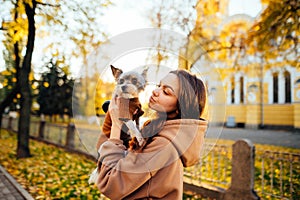 Portrait of a cute woman in casual clothes standing on the background on the background of autumn landscape with a small dog breed