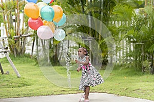 Portrait of cute young african girl hold funcy colour balloons in outdoor garden