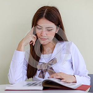 Portrait of cute and young Asian girl, Lao ethnicity, wearing Japanese, Korean style schoolgirl uniform, sitting and reading book