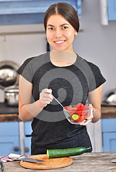 Portrait of cute young asian girl smiling while cooking salad with fresh vegetables in kitchen interior at home