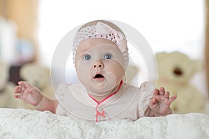 Portrait of a cute young baby wearing a bodysuit shirt lying on belly in nursery room