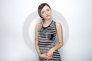 Portrait of cute young beautiful woman in striped shirt questioningly looking into camera posing for model tests against studio ba