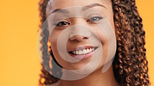 Portrait of cute young black lady with afro hairstyle smiling to camera, orange studio background, slow motion