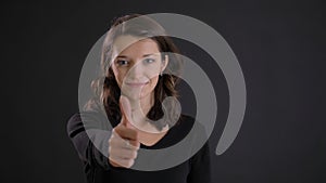 Portrait of cute young brunette woman gesturing finger-up sign smilingly to show like and respect on black background. photo